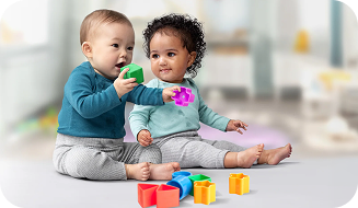 One baby observing as another infant places a green playing block into their mouth.