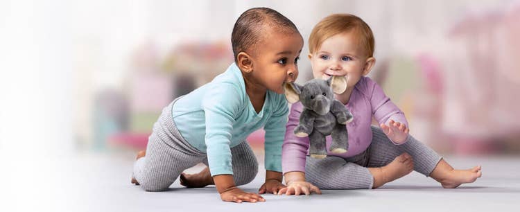 Two infants holding a toy elephant by its ears in their mouths.