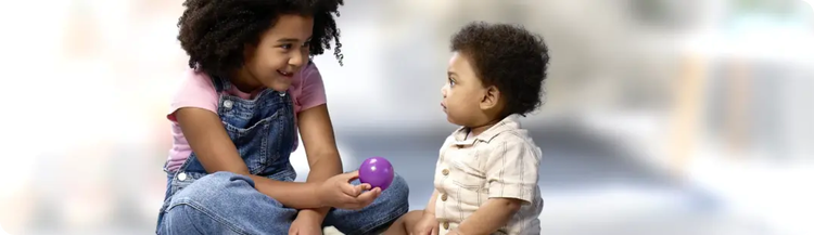 A young child showing a toddler a purple ball.