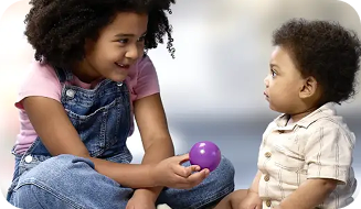 A young child showing a toddler a purple ball.