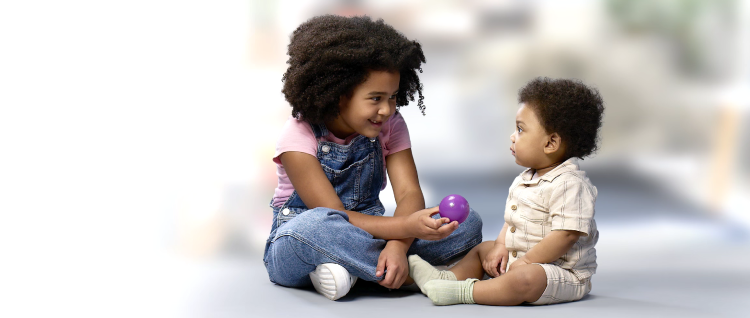 A young child showing a toddler a purple ball