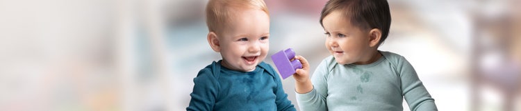 A baby passing a purple playing block to another infant.