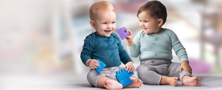 A baby passing a purple playing block to another infant.