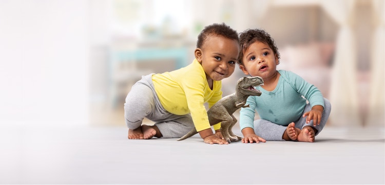 Two infants engaging in play with a dinosaur toy on the floor.